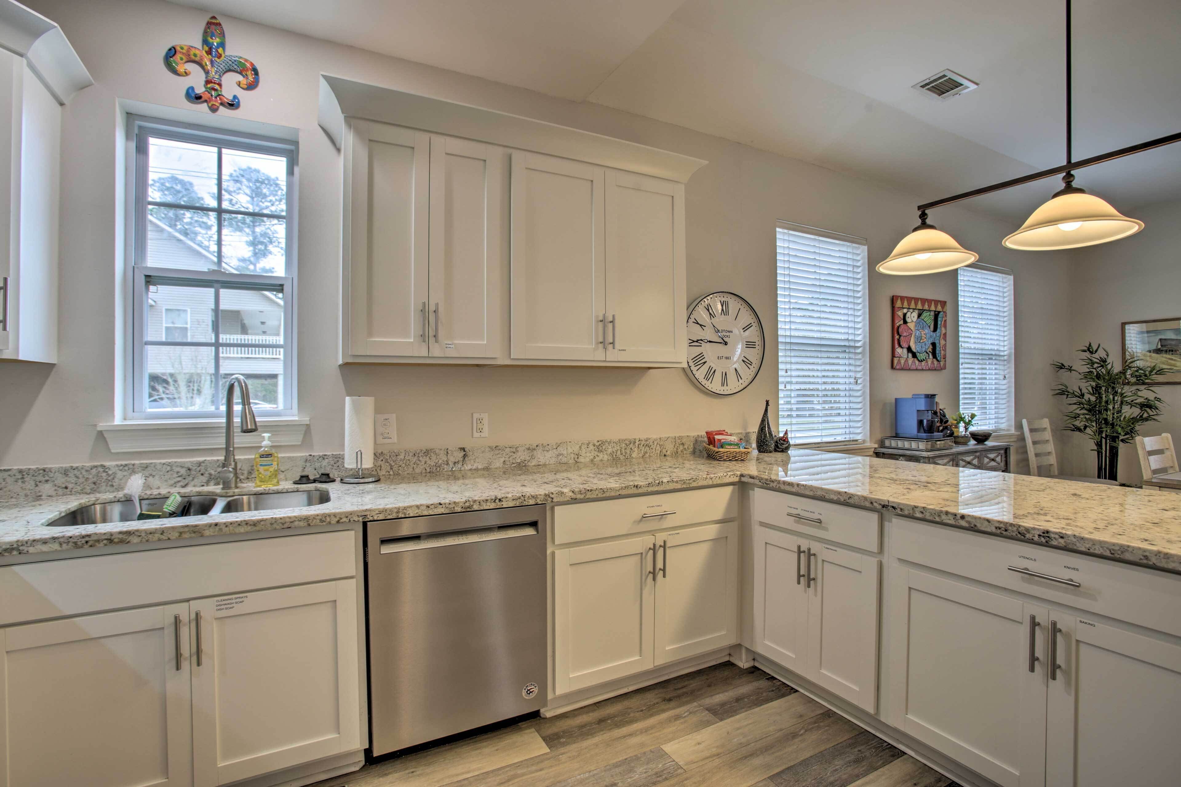 A modern kitchen with white cabinetry, a stainless steel dishwasher, a granite countertop, and pendant lighting.