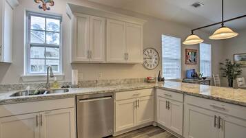 A modern kitchen with white cabinetry, a stainless steel dishwasher, a granite countertop, and pendant lighting.