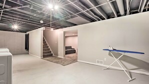 A spacious room with a concrete floor, a white wall, and a blue ironing board. - Homey Duplex - 10 Mi to Downtown Grand Rapids! (Jenison)