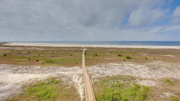 Un long sentier rectiligne menant à une plage, avec un ciel dégagé au-dessus.