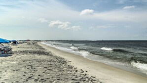 A beach with footprints leading to the water, a pier in the distance, and a clear sky.