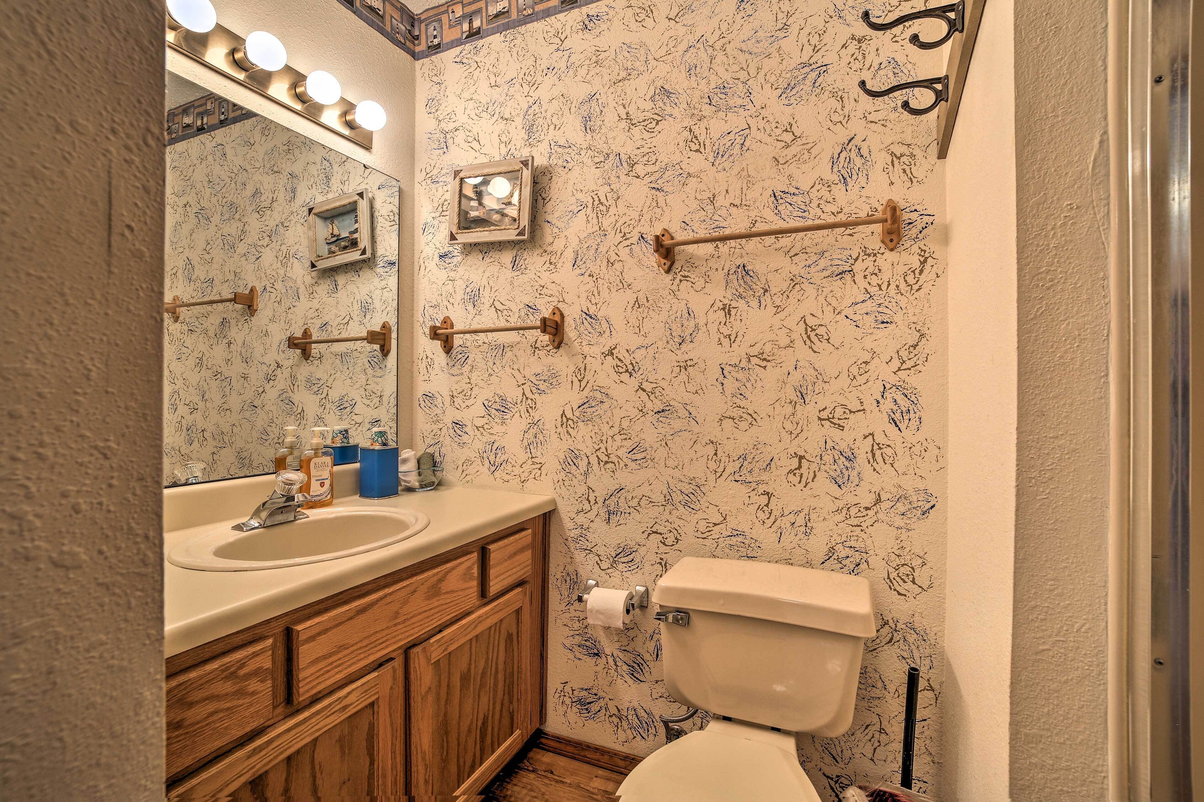 Un baño con tocador de madera, un lavamanos, un espejo con luces, un inodoro y una pared con estampado floral.