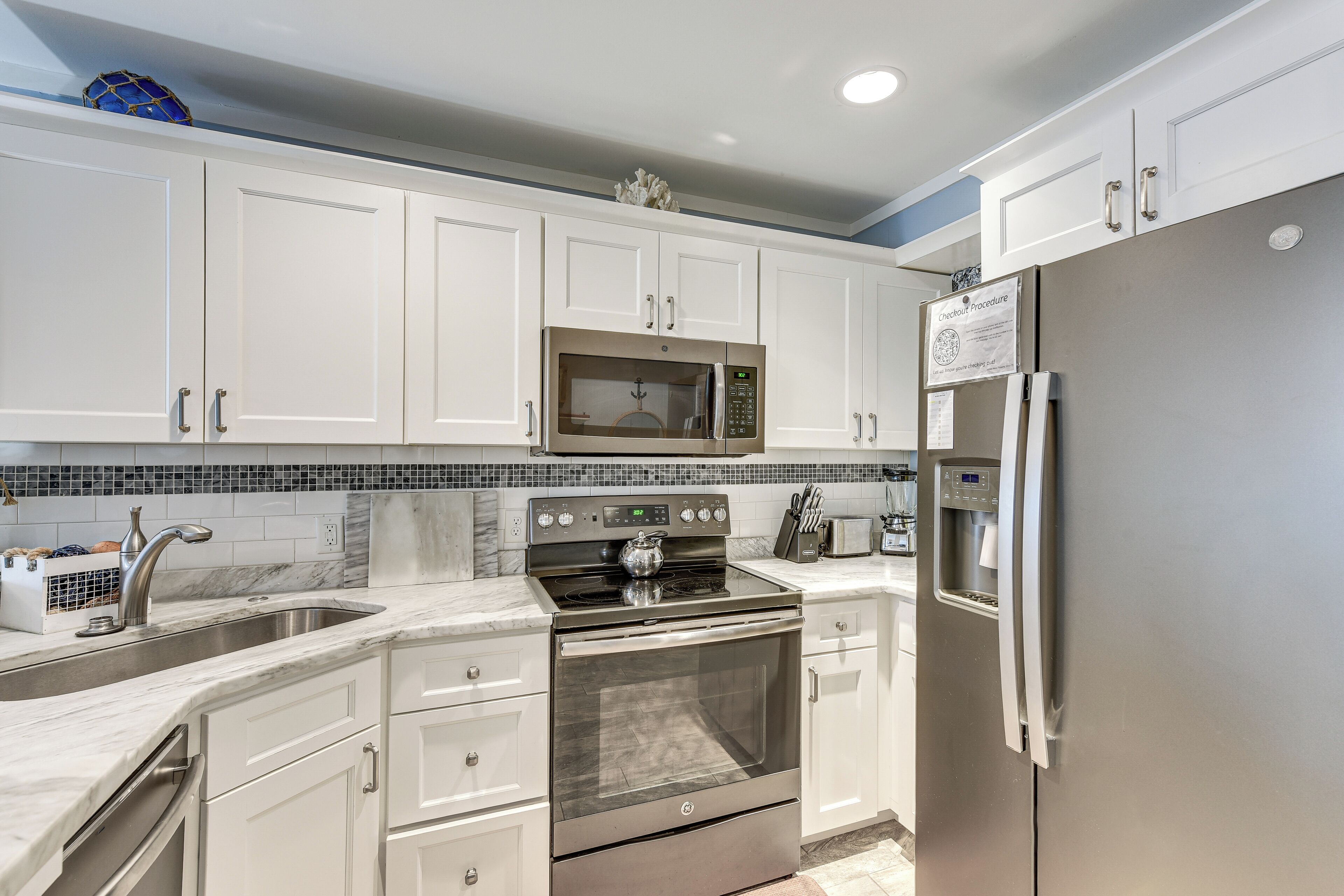A modern kitchen with white cabinets, a stainless steel refrigerator, a microwave, and an oven.