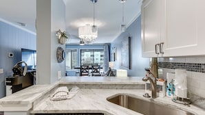 A modern kitchen with a marble countertop, stainless steel sink, and a built-in dishwasher. There is a dining area visible in the background with a table and chairs. - Walk to Beach: Hilton Head Resort Condo w/ Pools! (Hilton Head Island)