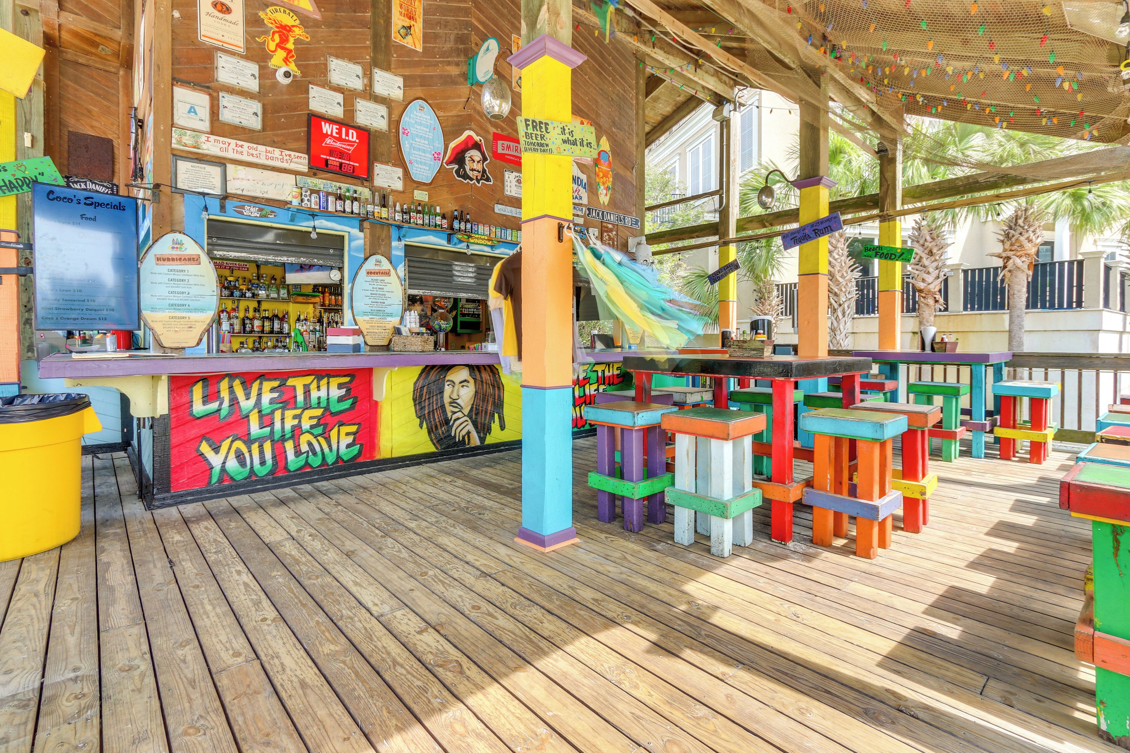 A colorful outdoor bar area with a wooden deck, a bar counter, and various signs and decorations.