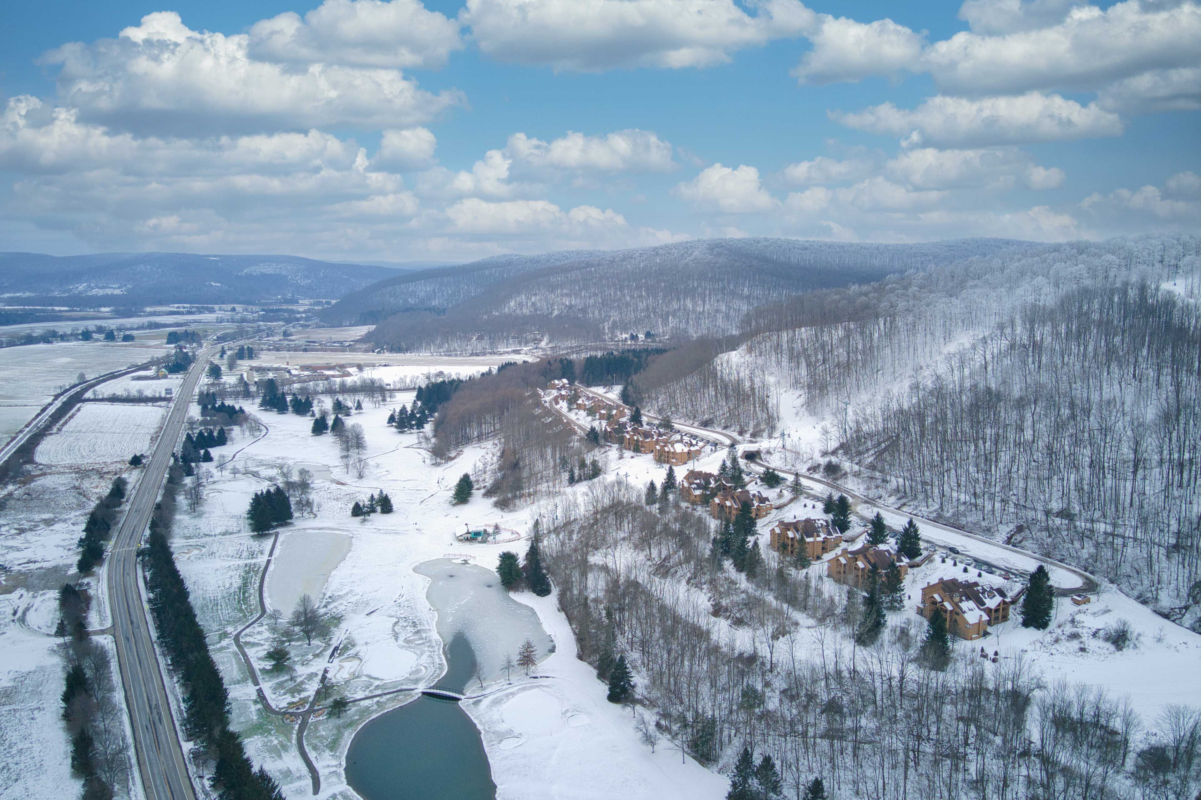 An aerial view of a snow-covered landscape with a residential area, roads, and a lake.