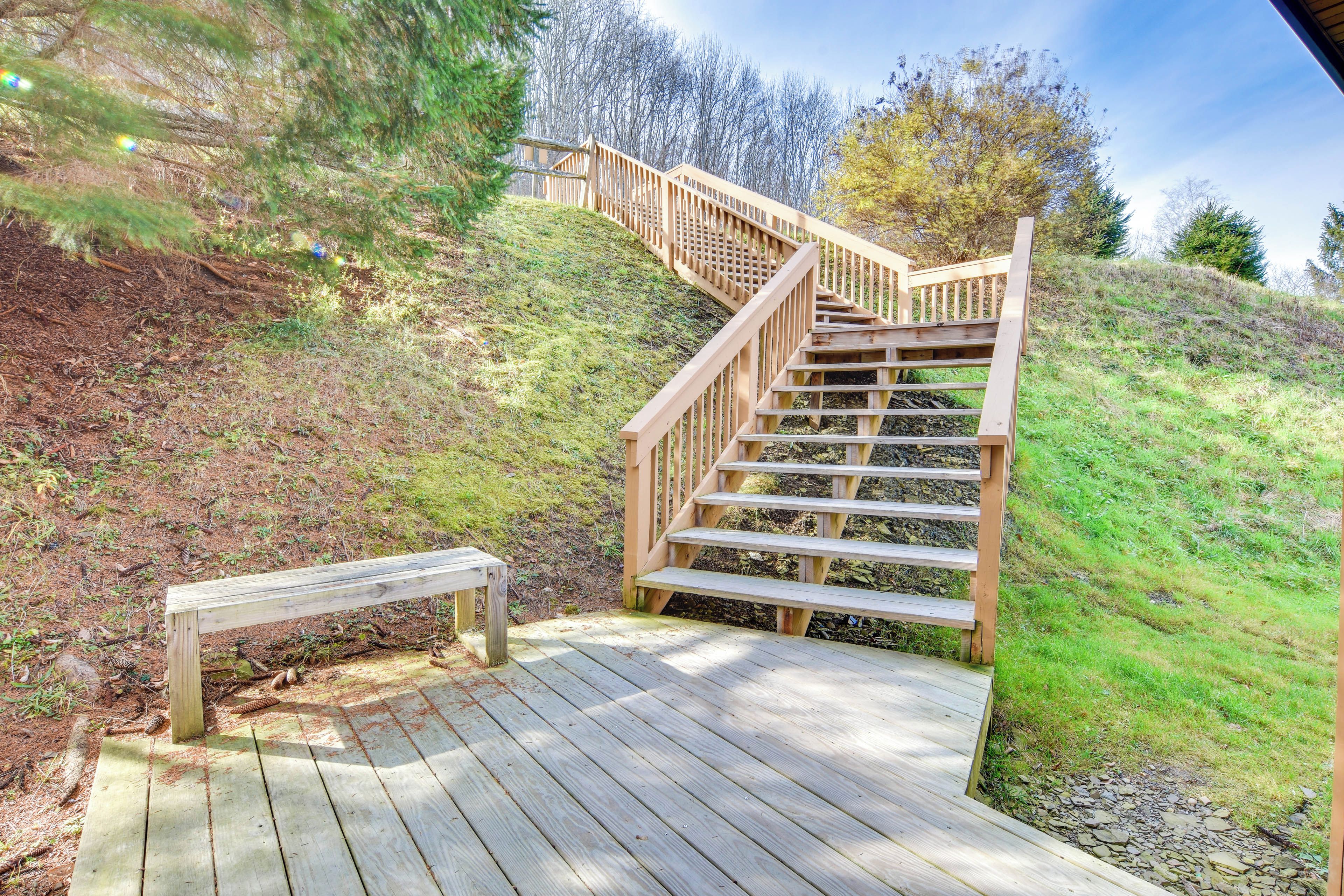 A wooden staircase leading up a grassy hill with a bench at the bottom.