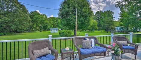 A deck with wicker furniture and a glass table, overlooking a well-maintained lawn and trees.