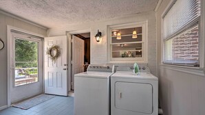 Une buanderie équipée de deux machines à laver et deux sèche-linge superposés, une porte décorée d’une guirlande et une fenêtre avec des stores.