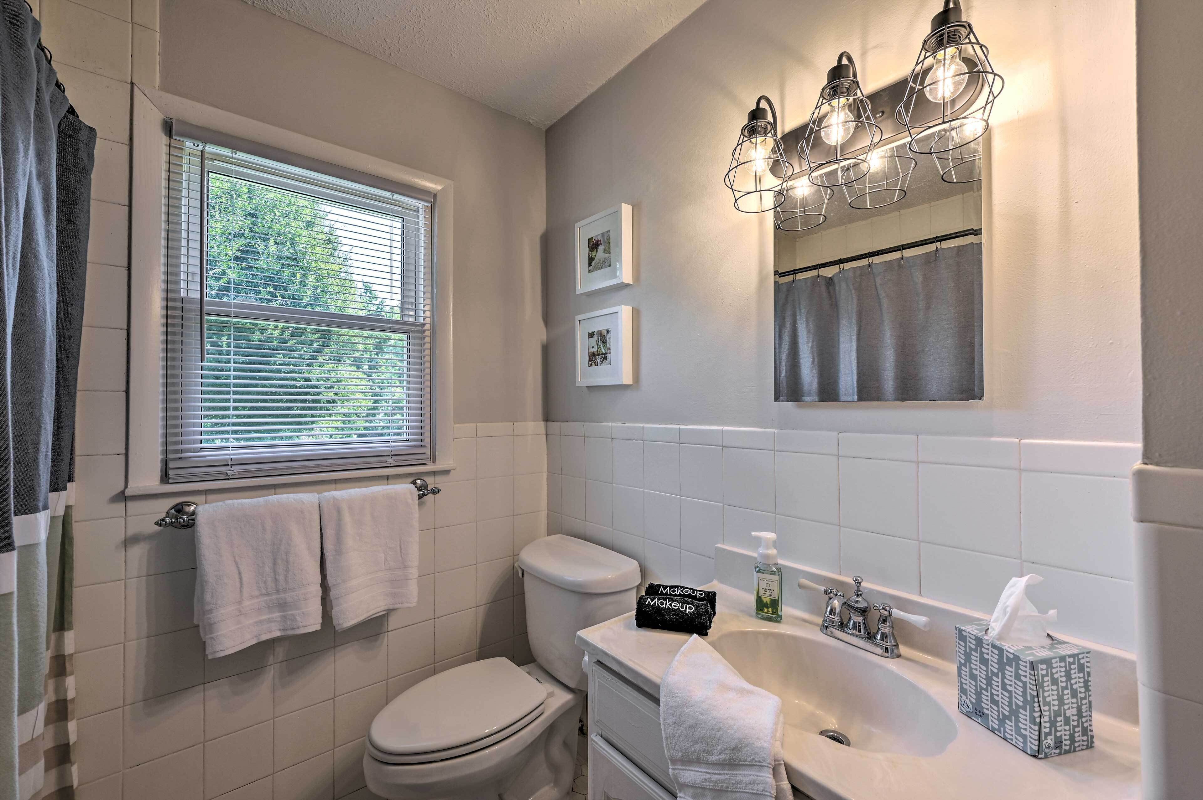 A bathroom with a toilet, sink, and window with blinds. There are towels hanging on the wall and a makeup bag on the sink.