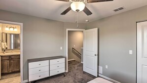 Une chambre à coucher comprenant un lit, une commode, un ventilateur de plafond et une salle de bain avec un lavabo et un miroir.