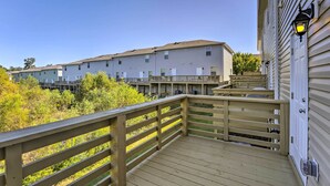 Une terrasse en bois avec des garde-corps, un bâtiment doté de nombreuses fenêtres et un ciel dégagé.