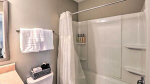 Une salle de bain avec une douche à parois de verre, des toilettes dotées d’un compartiment de rangement et un porte-serviettes avec plusieurs serviettes.