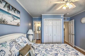 A bedroom with a bed, a ceiling fan, a door, and a wall with a painting.