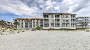 Een hotel aan het strand met meerdere verdiepingen, balkons en een zandstrand op de voorgrond.