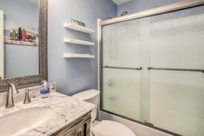A bathroom with a marble sink, a toilet, a glass shower enclosure, and a shelf with toiletries.