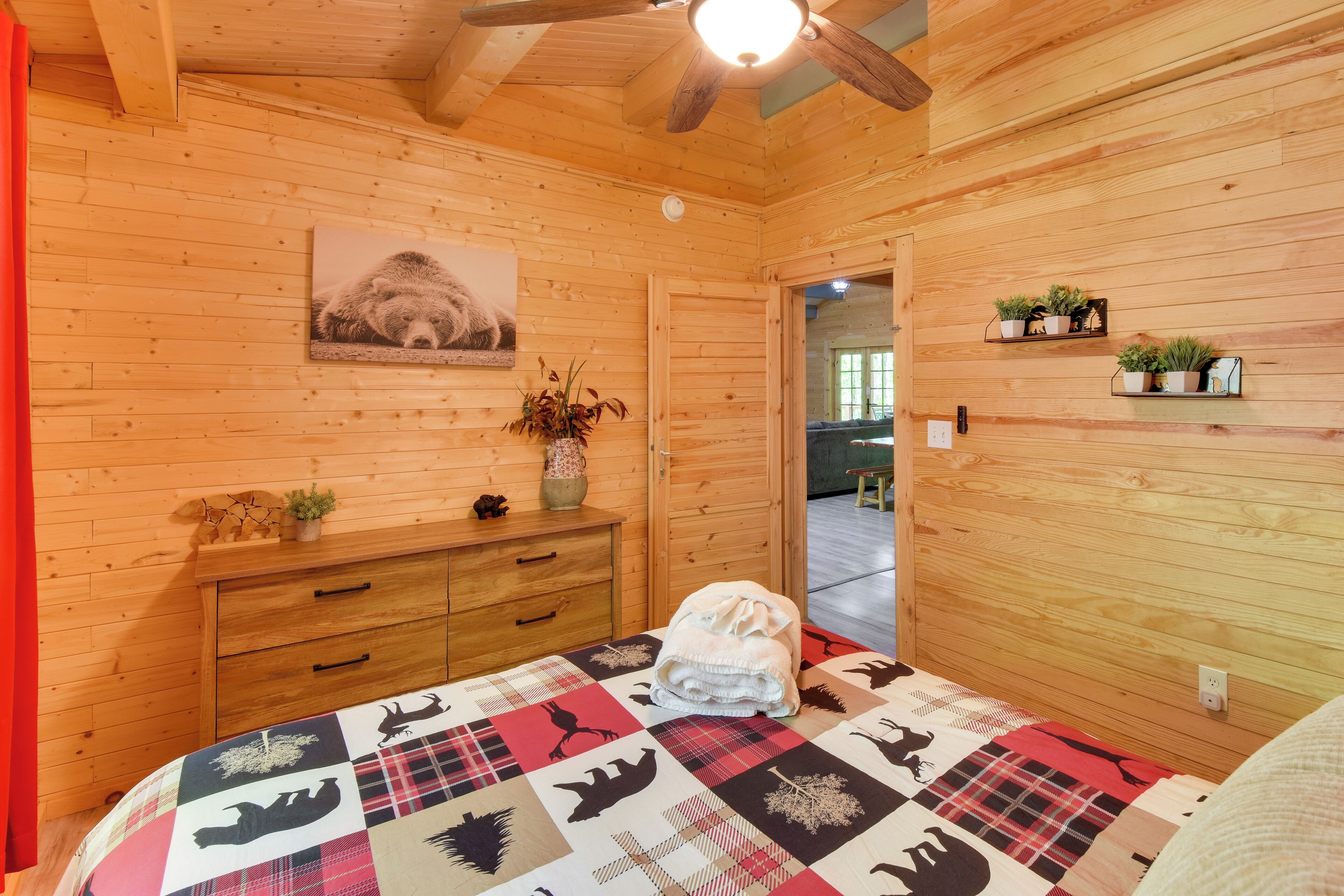 Un dormitorio de cabaña de madera con cama, cómoda, un cuadro y un pasillo que conduce a otra habitación.
