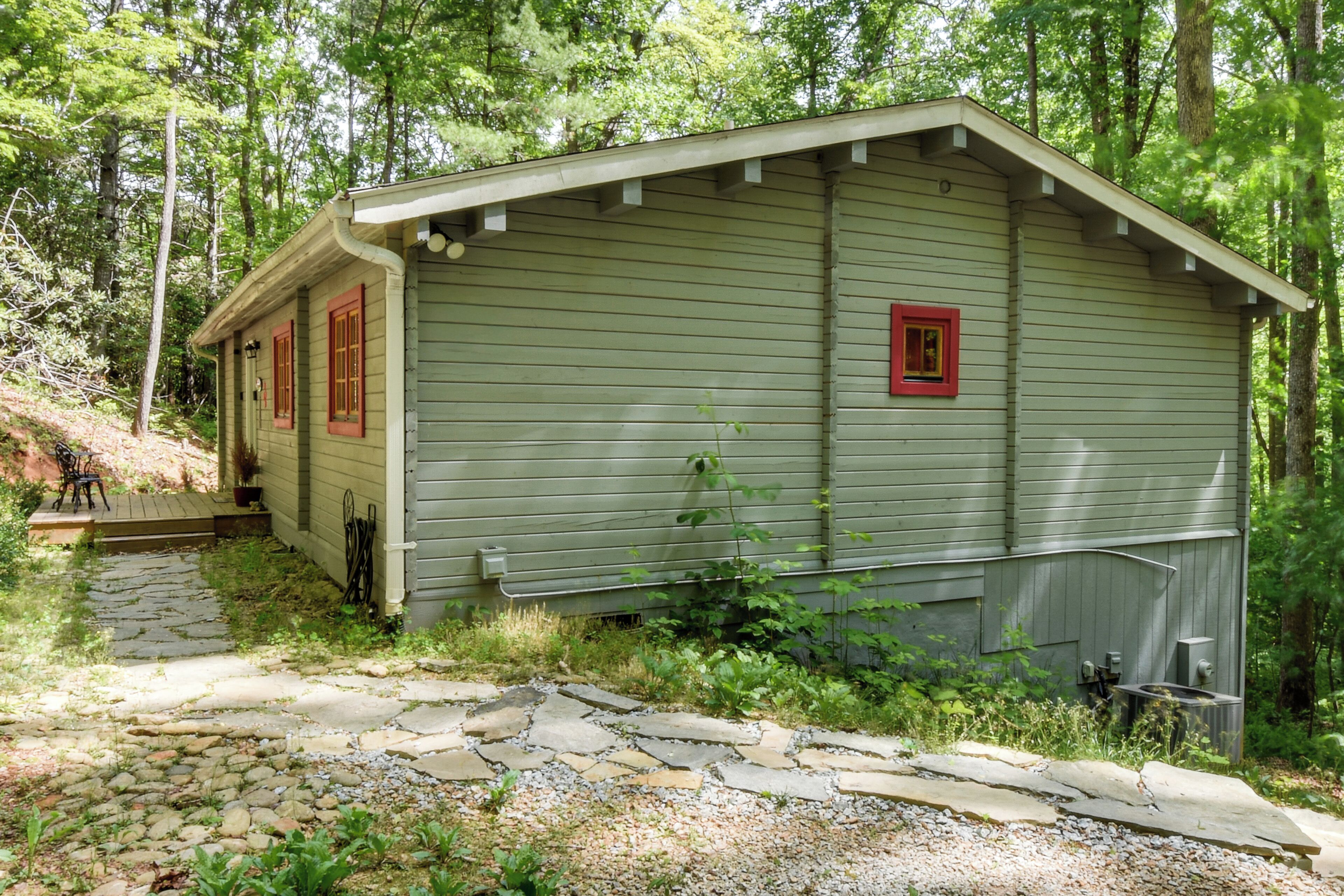 A small, single-story cabin with a stone pathway leading to the entrance, surrounded by dense forest.