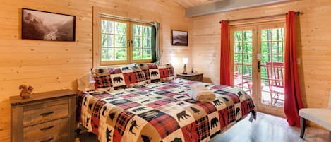 A wooden cabin bedroom with a bed, nightstand, and windows.