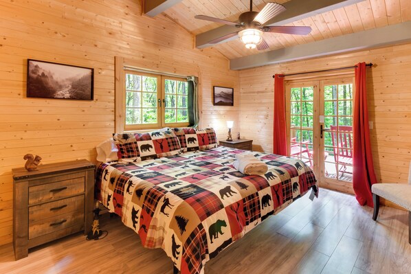 Un dormitorio de cabaña de madera con cama, mesita de noche y ventanas.