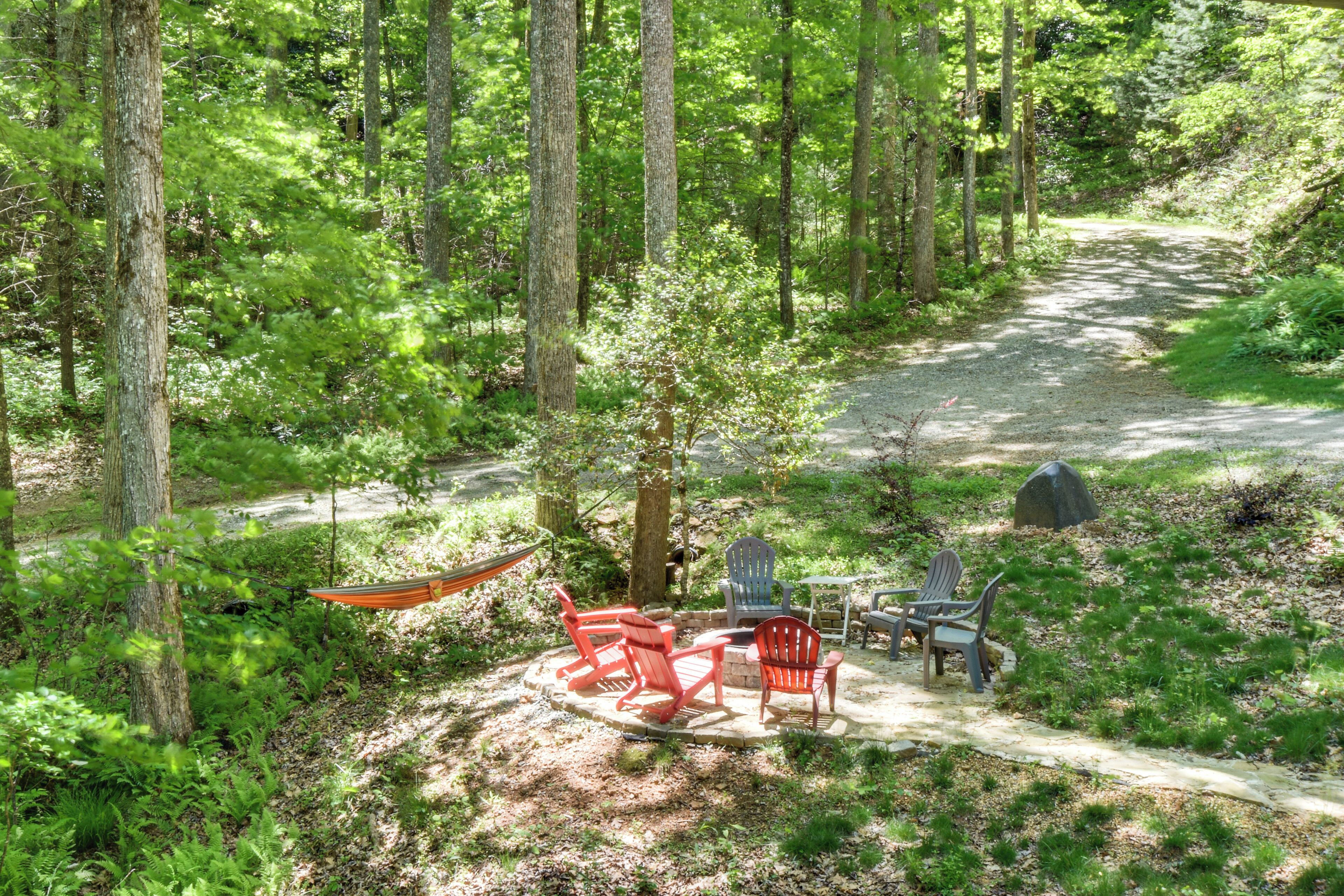 Ett skogsområde med en grusgång, röda Adirondack-stolar, en blå Adirondack-stol och en hängmatta.