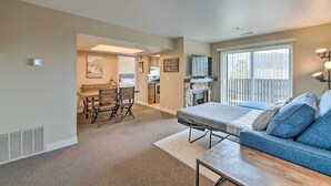 A spacious living room with a large window, a sofa, a dining table, and a kitchen area in the background. - Walkable Park City Condo w/ Pool & Hot Tub! (Park City)