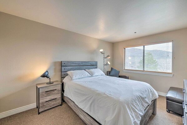 A bedroom with a bed, bedside tables, a lamp, and a window with blinds.