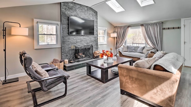 A modern living room with a stone fireplace, a flat-screen TV, and a cozy seating area with a sofa and armchairs. - Hot Tub & Fire Pit: Modern Pocono Mountain Home (Pocono Lake)