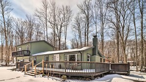 A two-story house with a deck, surrounded by trees and snow. - Hot Tub & Fire Pit: Modern Pocono Mountain Home (Pocono Lake)