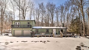 A two-story cabin with a balcony and a deck, surrounded by a snowy landscape and trees. - Hot Tub & Fire Pit: Modern Pocono Mountain Home (Pocono Lake)