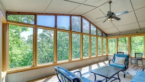 A sunroom with large windows, a ceiling fan, and seating areas. - The Bella Vista Lakeside Treehouse: Dock & Kayaks! (Bella Vista)