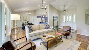 A spacious living room with a sofa, chairs, a coffee table, and a dining area in the background. - The Bella Vista Lakeside Treehouse: Dock & Kayaks! (Bella Vista)