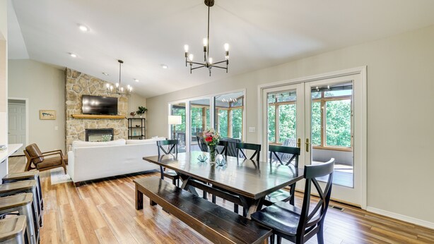 A spacious living room with a large wooden dining table, a stone fireplace, and a modern chandelier. - The Bella Vista Lakeside Treehouse: Dock & Kayaks! (Bella Vista)