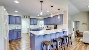 A modern kitchen with blue cabinets, a large island, and bar stools. - The Bella Vista Lakeside Treehouse: Dock & Kayaks! (Bella Vista)