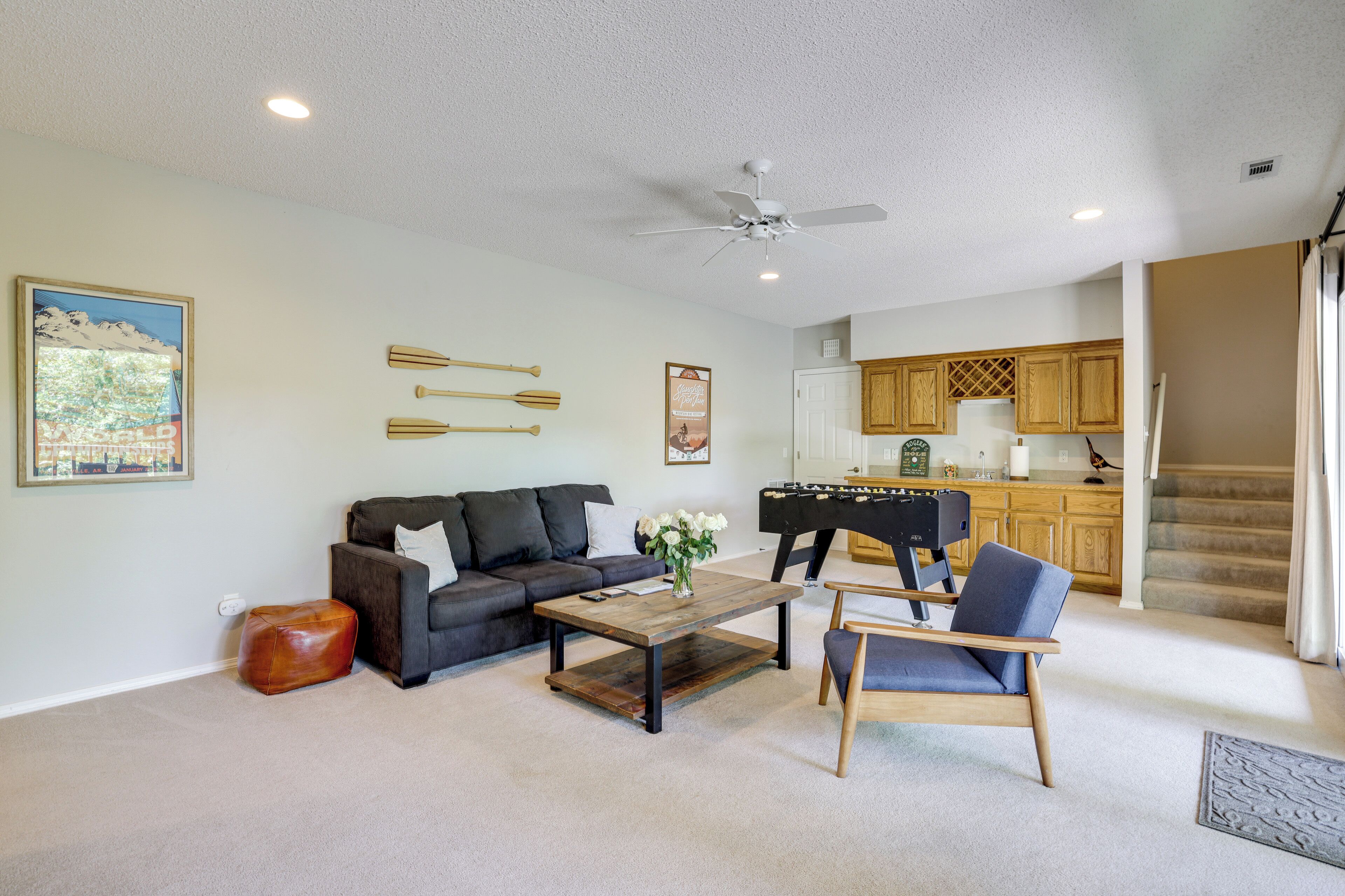 A living room with a sofa, coffee table, and armchair, a kitchen in the background, and a ceiling fan.