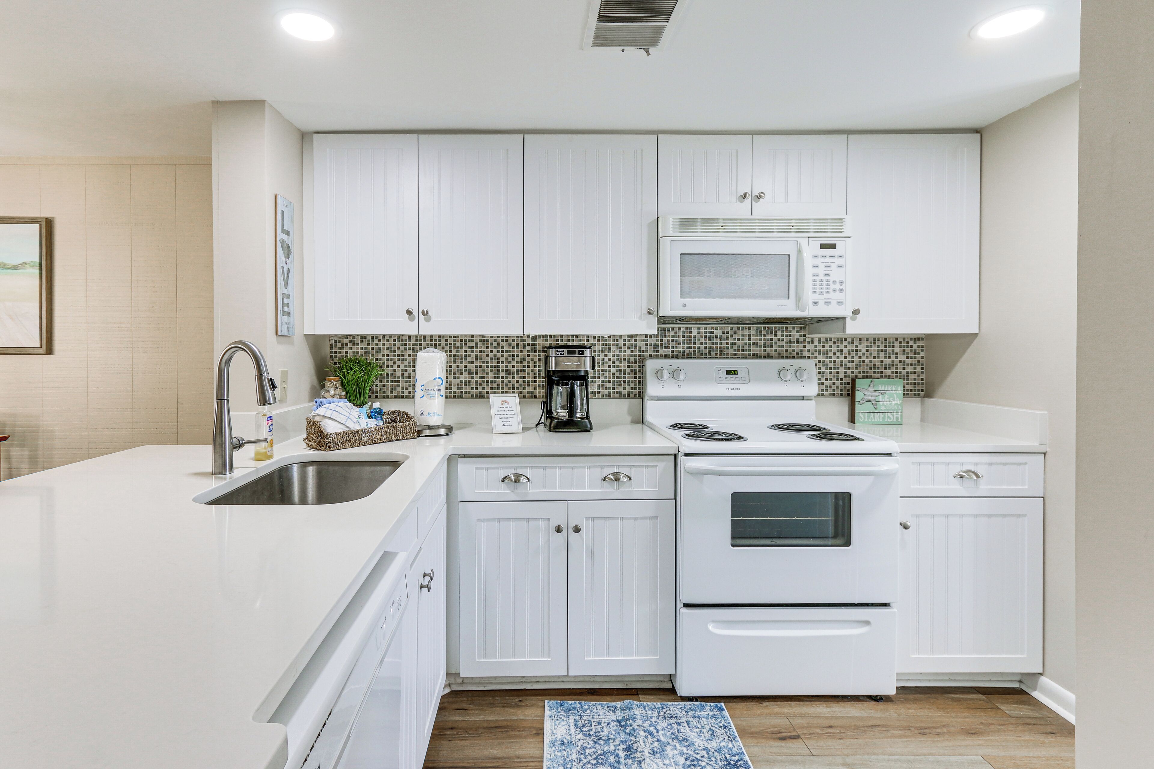 A modern kitchen with white cabinetry, a built-in microwave, a stove, and a sink.