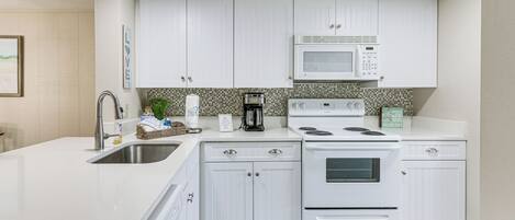 A modern kitchen with white cabinetry, a built-in microwave, a stove, and a sink.