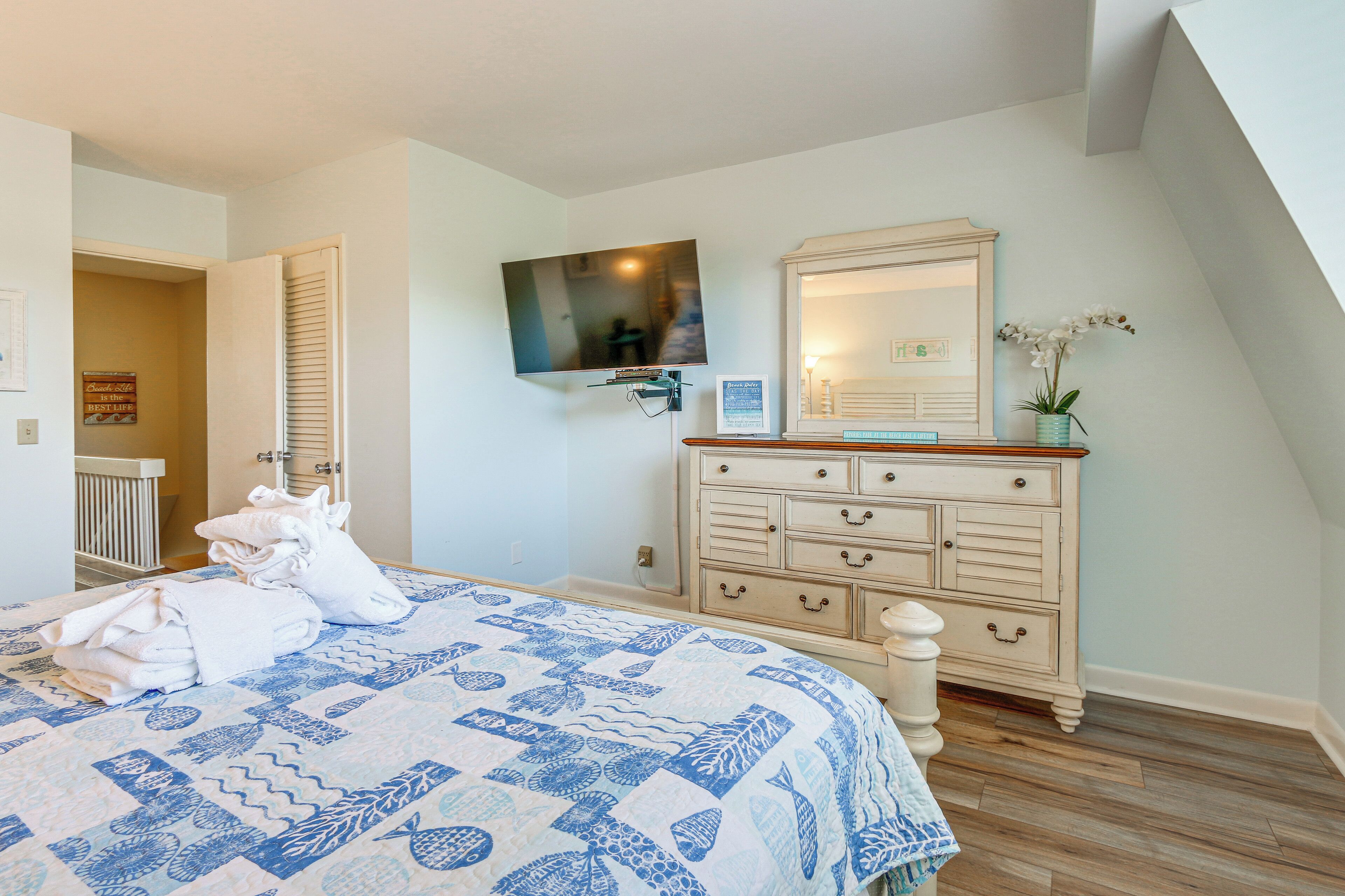 Un dormitorio con cama, cómoda, televisor y puerta que da a otra habitación.