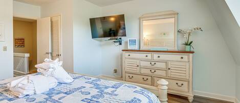 Un dormitorio con cama, cómoda, televisor y puerta que da a otra habitación.
