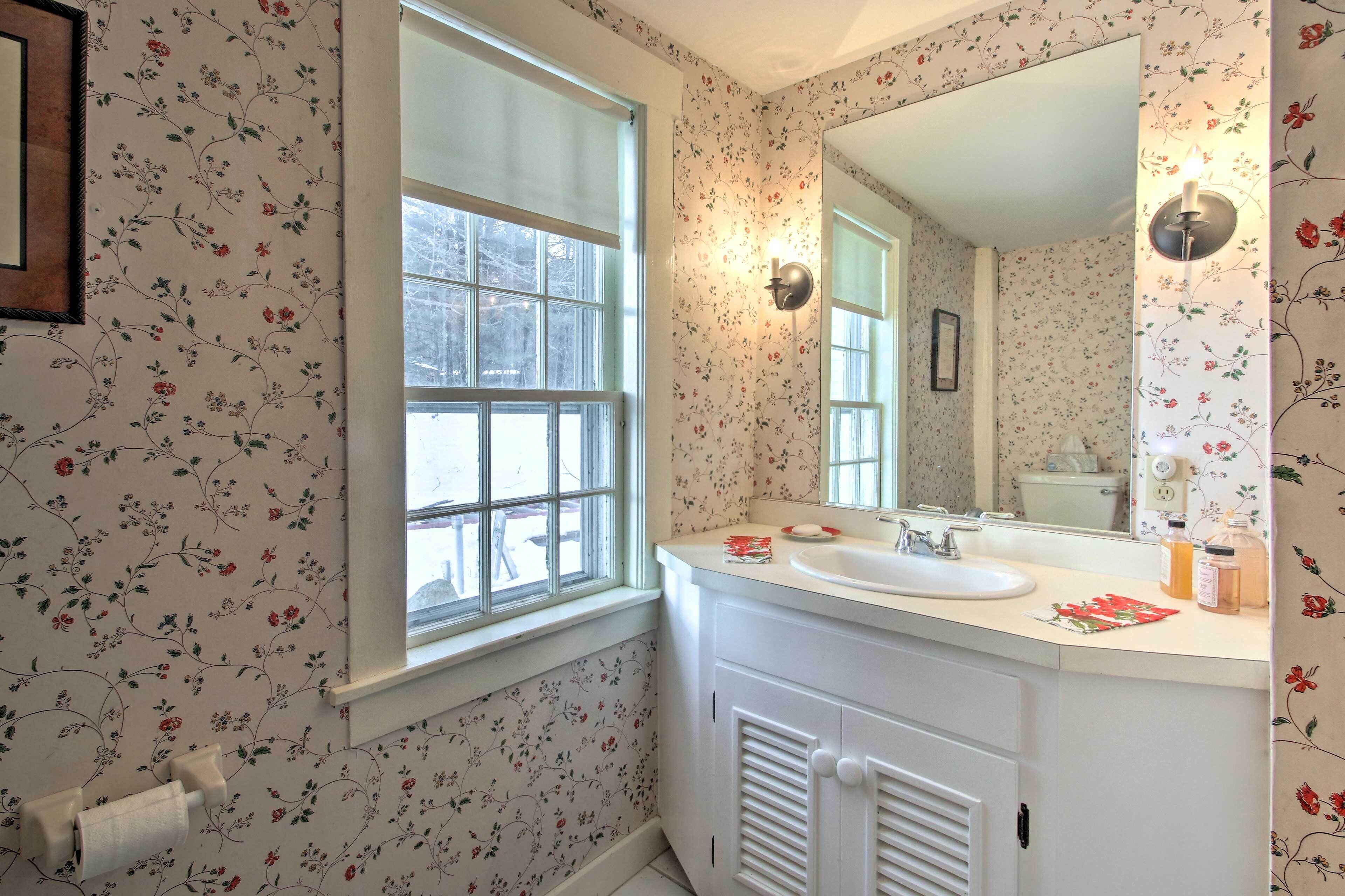 A bathroom with floral wallpaper, a window, a sink, and a mirror.