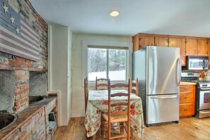 Eine Küche mit Backsteinwand, Holzausbau und einem Edelstahl-Kühlschrank, einer Mikrowelle sowie einem Tisch mit Blumenmuster-Tischdecke.