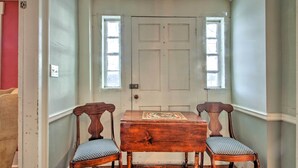 Una stanza con una porta bianca, due sedie di legno con sedili imbottiti e un piccolo tavolo in legno con un oggetto decorativo sopra.