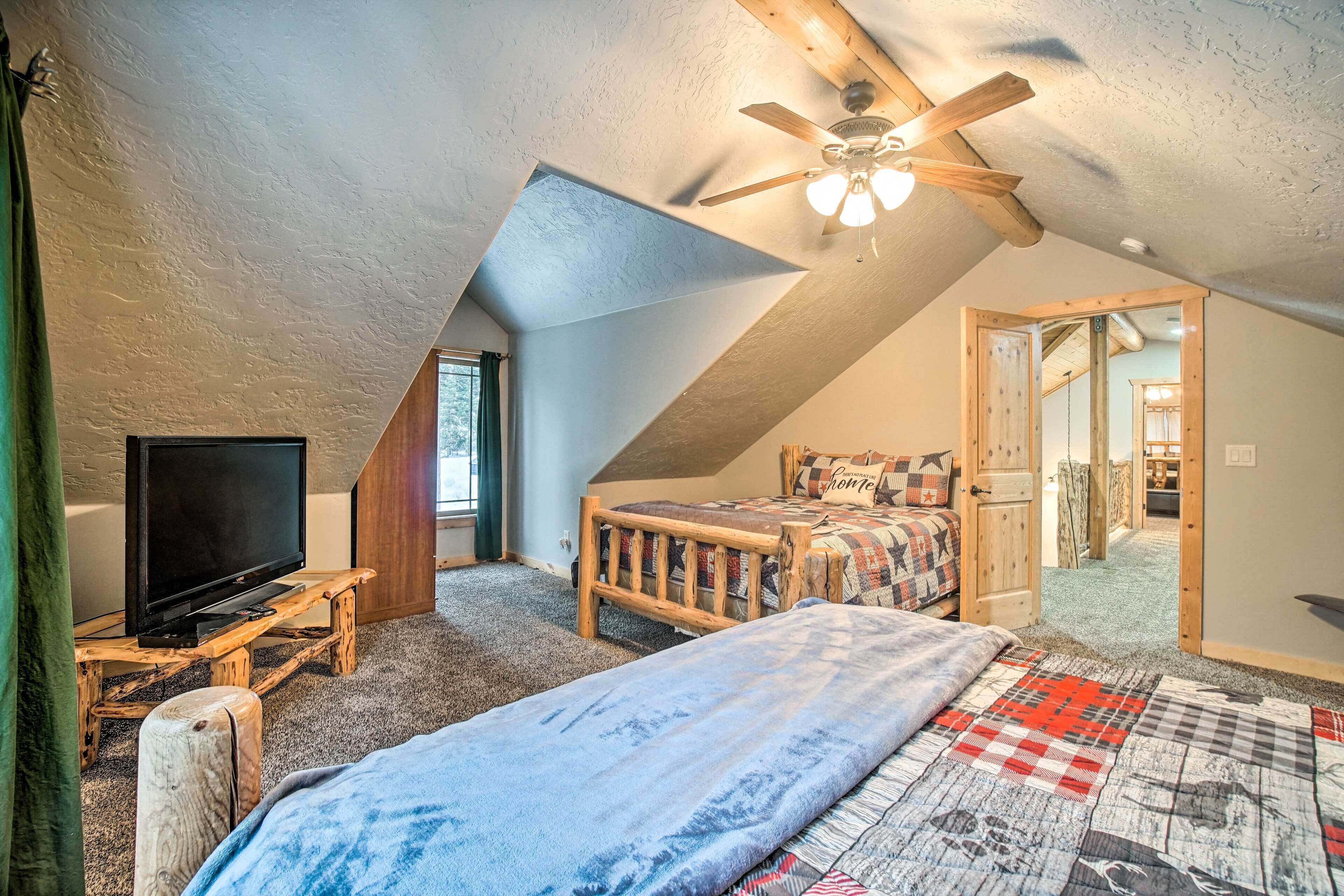 A cozy attic bedroom with a sloped ceiling, a ceiling fan, a bed with a quilt, a wooden bench, and a television on a stand.