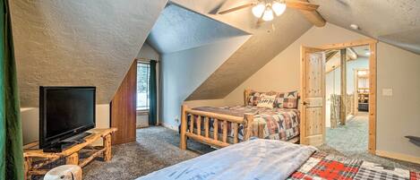 A cozy attic bedroom with a sloped ceiling, a ceiling fan, a bed with a quilt, a wooden bench, and a television on a stand.