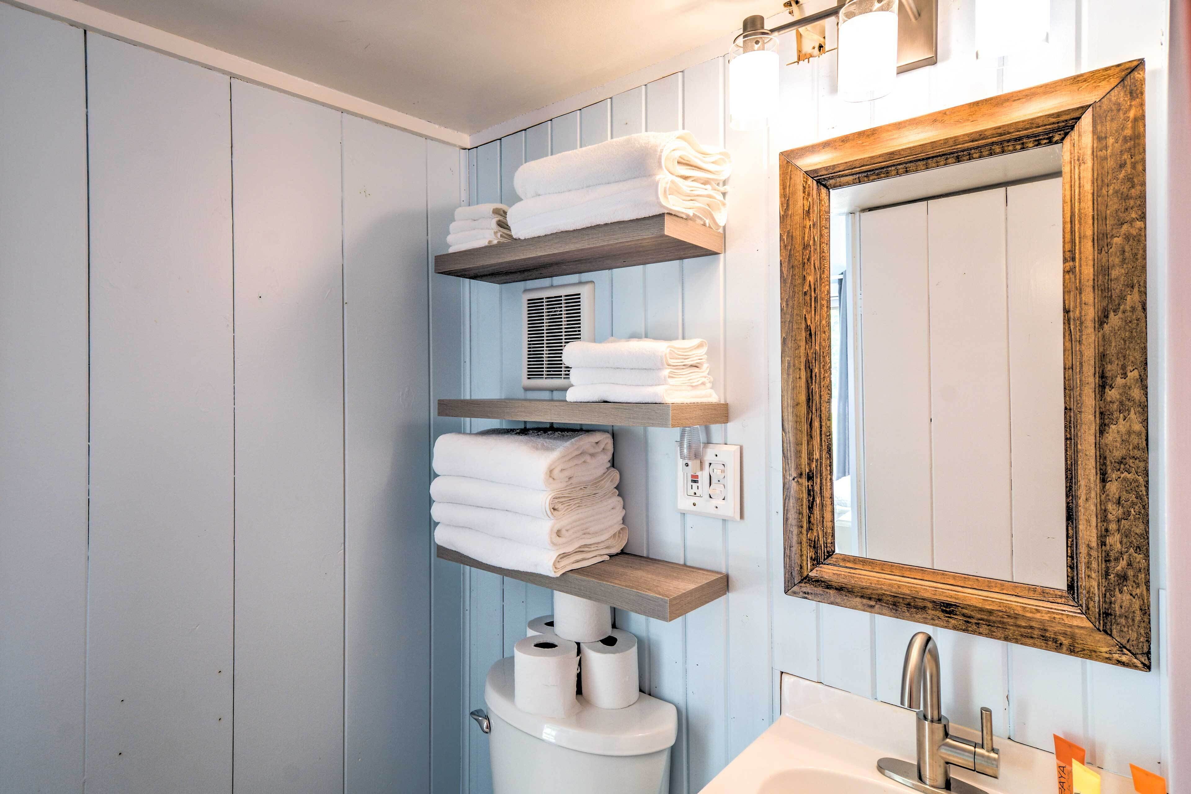 A bathroom with wooden shelves holding towels, a toilet, and a sink with a mirror.