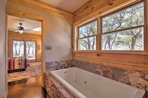 A bathroom with a large bathtub, wooden walls, and a window with a view of trees. - Twin Acres Scenic Ranch in Texas Hill Country (Florence)