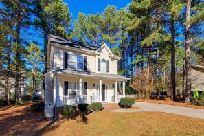 A two-story house with a front porch, surrounded by tall pine trees. - Wendell Home w/ Fenced Yard, Close to Raleigh (Wendell)