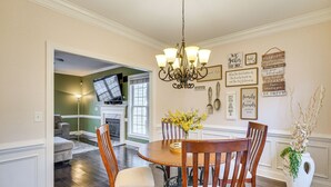 A dining area with a chandelier, wooden chairs, a round table, and a vase of flowers. - Wendell Home w/ Fenced Yard, Close to Raleigh (Wendell)