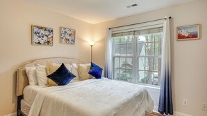 A bedroom with a large bed, a nightstand, a floor lamp, and a window with curtains. - Wendell Home w/ Fenced Yard, Close to Raleigh (Wendell)