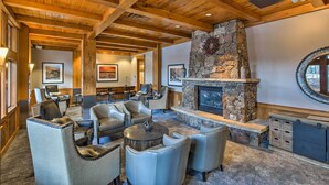 A cozy lounge area with leather chairs, a stone fireplace, and wooden beams on the ceiling.
